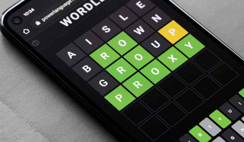 Jocul Wordle, pe un telefon negru, care stă pe un fundal gri. Wordle a fost cumpărat recent