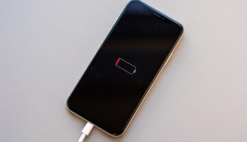 iPhone cu bateria scursă, băgat la încărcat, pe un fundal gri. Actualizarea iOS 15.4 ar afecta bateria dispozitivelor iPhone