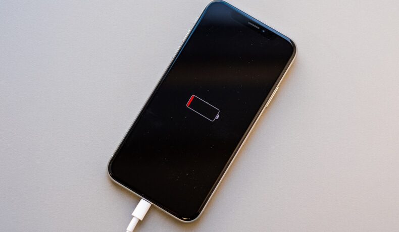 iPhone cu bateria scursă, băgat la încărcat, pe un fundal gri. Actualizarea iOS 15.4 ar afecta bateria dispozitivelor iPhone