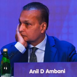 Anil Ambani, 2019, Mumbai, la un eveniment Reliance ADAG Companies. Poartă un costum albastru, pe un fundal albastru, cu o etichetă cu numele lui. Anil Ambani a pierdut o avere de 42 de miliarde de dolari