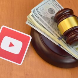 Logoul YouTube, lângă ciocănelul unui judecător, cu bani pe el, pe fundal de lemn. Bungie a intentat recent un proces din cauza regulilor YouTube