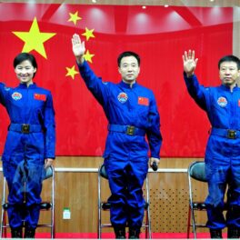 Liu Yang și colegii săi din misiunea Shenzhou IX, 2012, toți 3 ămbrăcați în costum albastru, cu steagul Chinei roșu pe fundal. China va deschide stația spațială Tiangong pentru turiști