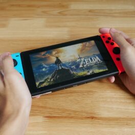 Joc The Legend of Zelda pe un Nintendo Switch, ținut în mână de un utilizator, pe un fundal de lemn deschis. Continuarea The Legend of Zelda: Breath of The Wild va fi lansată în 2023