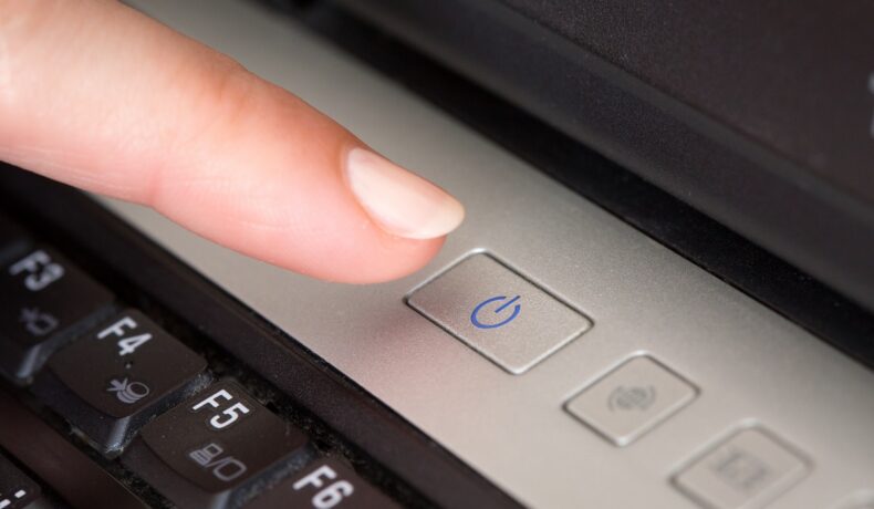 Degetul unui utilizator care închide un laptop Windows, cu butonul de închidere. Mulți se întreabă cum trebuie să închizi computerul Windows