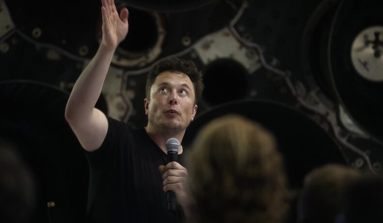 Elon Musk, 2018, în cadrul unei prezentări spațiale. E îmbrăcat într-un tricou negru, cu microfon în mână. Elon Musk ar putea deveni primul trilionar din istorie