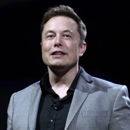 Elon Musk pe scenă, îmbrăcat într-un costum gri, cu o cămașă neagră, pe fundal negru. Elon Musk vrea să se implice într-o nouă industrie