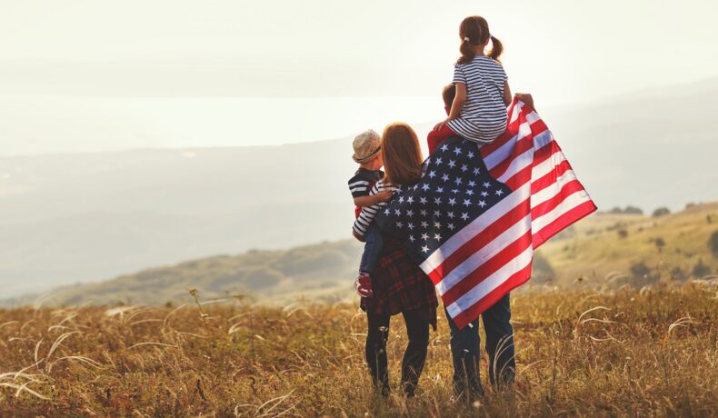 Familie cu 2 părinți și 2 copii, cu steagul american, care stau pe un deal și se uită la apus. Expunerea la plumb ar fi redus IQ-ul populației SUA