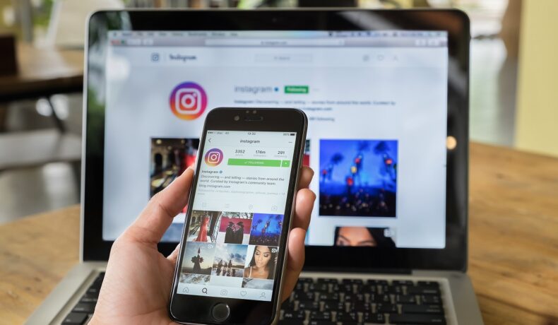 Utilizator care are telefon în mână, cu Instagram pe ecran, și pe fundal, pe ecranul unui laptop. Instagram revine la afișarea cronologică a imaginilor în 2022