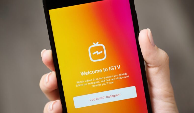 Utilizator care are un telefon în mână, cu aplicația IGTV portocalie pe ecran. Instagram a anunțat că va închide aplicația IGTV
