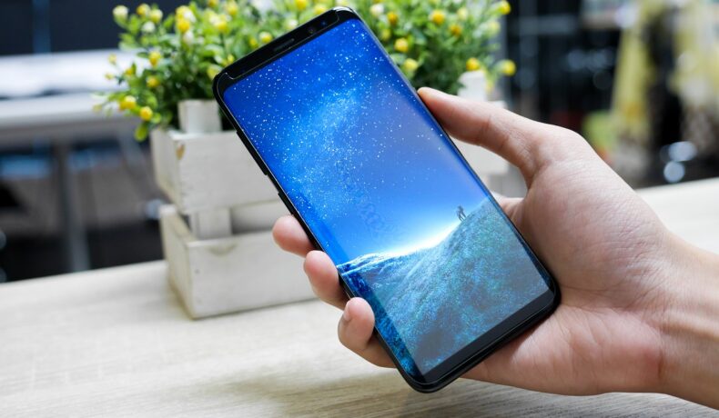 Samsung Galaxy S8, în mâna unui utilizator, cu imagine albastră pe ecran. Samsung Awesome Galaxy A va avea loc pe 17 martie 2022