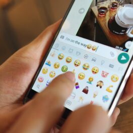 Emojiuri WhatsApp, pe un telefon, ținut în mână de un utilizator. WhatsApp introduce reacții cu emoji în mesaje în curând