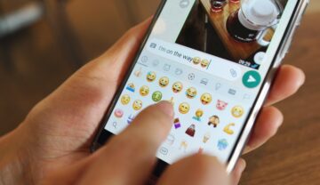 Emojiuri WhatsApp, pe un telefon, ținut în mână de un utilizator. WhatsApp introduce reacții cu emoji în mesaje în curând