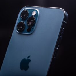 Un telefon iPhone 12 Pro pe albastru, cu fundal negru și logo-ul Apple pe spate. O sursă a dezvăluit recent cât ar putea costa iPhone 14