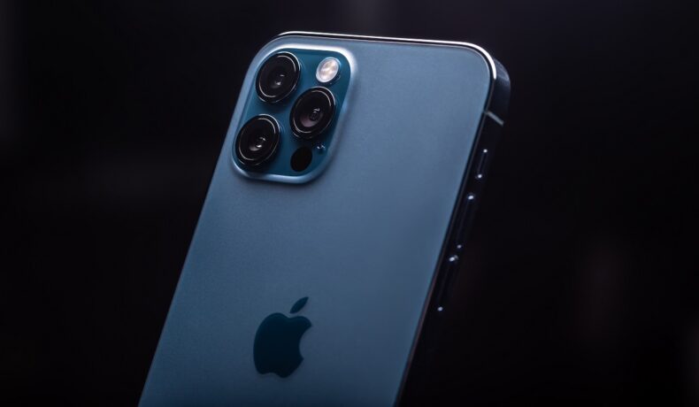 Un telefon iPhone 12 Pro pe albastru, cu fundal negru și logo-ul Apple pe spate. O sursă a dezvăluit recent cât ar putea costa iPhone 14