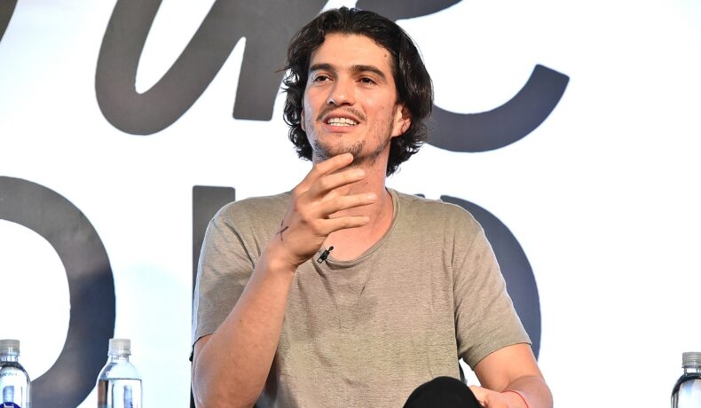 Adam Neumann, pe scenă în 2016, în cadrul unui eveniment iHeartMedia și WeWork, pe fundal alb cu negru, poartă cămașă bej. WeWork e compania lui Adam Neumann