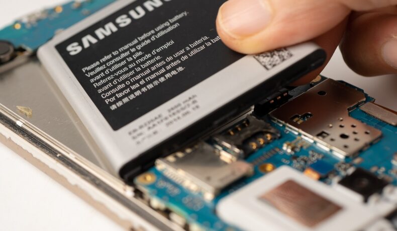 Utilizator care înlătură bateria unui telefon Samsung, pe fundal alb. Dispozitivele Galaxy vor putea fi reparate chiar de către utilizatori