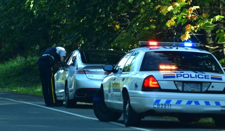 Mașină de poliție în spatele unei mașini trase pe dreapta pe un drum, cu un ofițer lângă vehicul. O mașină a fost oprită în trafic fără șofer
