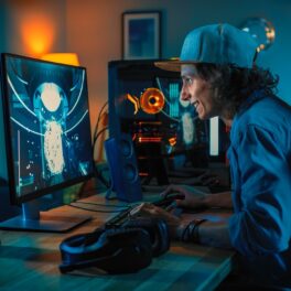 Un băiat care se joacă un joc pe calculator, stând la birou, pe fundal albastru. Seria Max Payne va fi refăcută în curând