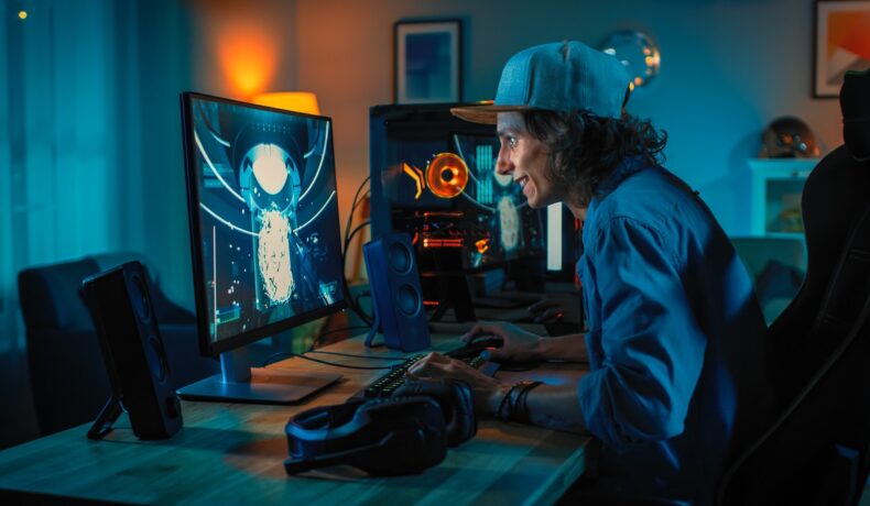 Un băiat care se joacă un joc pe calculator, stând la birou, pe fundal albastru. Seria Max Payne va fi refăcută în curând