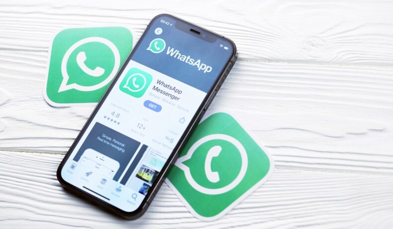 Telefon care are WhatsApp pe ecran, cu logo-urile whatsapp langa, pe fundal de lemn deschis la culoare. Toți utilizatorii WhatsApp sunt avertizați să șteargă mesajele periculoase
