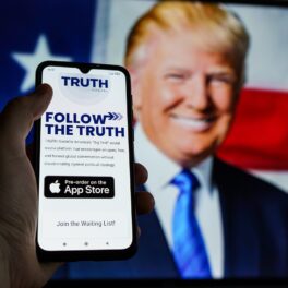 Truth Social, aplicația lui Donald Trump, pe ecranul unui telefon, cu fundal cu Trump și steagul american