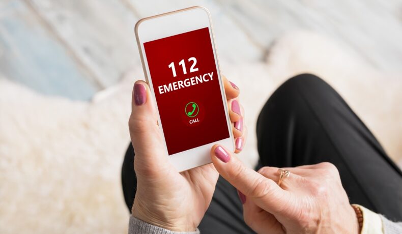 Femeie care ține în mână un telefon iPhone, ecran roșu, cu urgență 112 pe ecran. Un iPhone a salvat viața proprietarului său