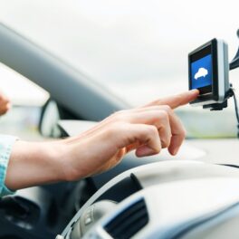 Bărbat care se află în mașină și apasă pe un ecran aflat deasupra volanului, unul dintre cele mai utile dispozitive pentru mașină