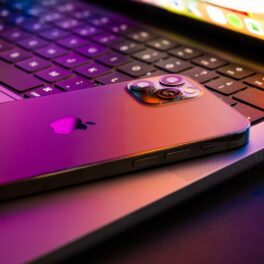 Un iPhone 13, cu spatele în sus, pe o tastatură MacBook, în culori mov și portocalii. Unele imagini pe Internet prezintă cum va arăta ecranul iPhone 14