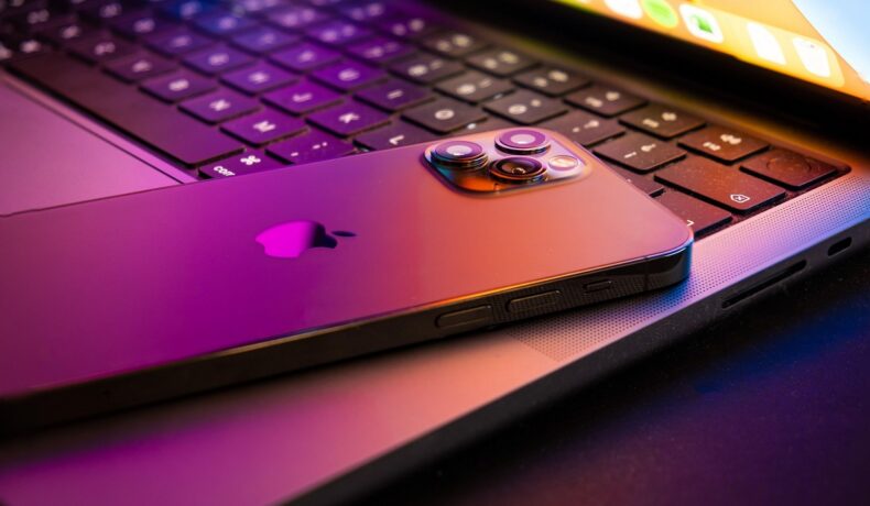 Un iPhone 13, cu spatele în sus, pe o tastatură MacBook, în culori mov și portocalii. Unele imagini pe Internet prezintă cum va arăta ecranul iPhone 14