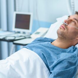 Bărbat care stă în pat de spital, îmbrăcat în albastru, care se uită în sus. Experții au descoperit recent noi indicii despre ce cauzează cancerul
