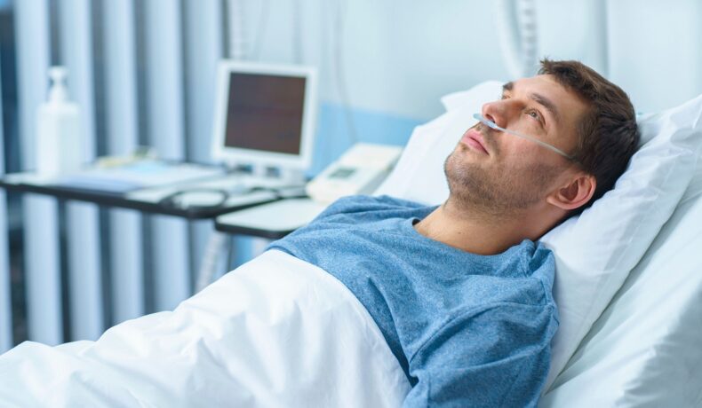 Bărbat care stă în pat de spital, îmbrăcat în albastru, care se uită în sus. Experții au descoperit recent noi indicii despre ce cauzează cancerul
