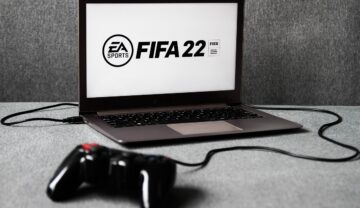 Laptop negru cu FIFA 22 pe ecranul alb, cu fundal gri. FIFA 22 include un echipament cu motive românești