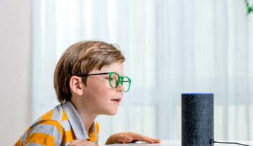 Un copil cu ochelari care vorbește cu Alexa, care va putea imita vocile rudelor decedate