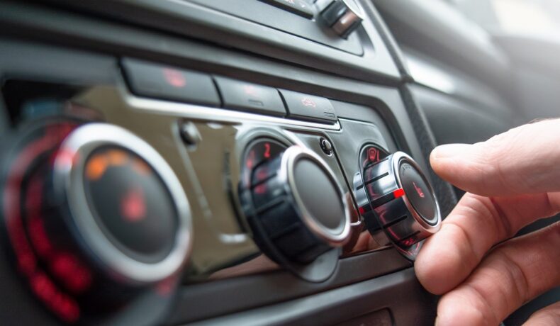 Șofer care își îndreaptă mână spre butonul din mașină legate de aerul condiționat, care te poate ajuta la reducerea consumului de combustibil