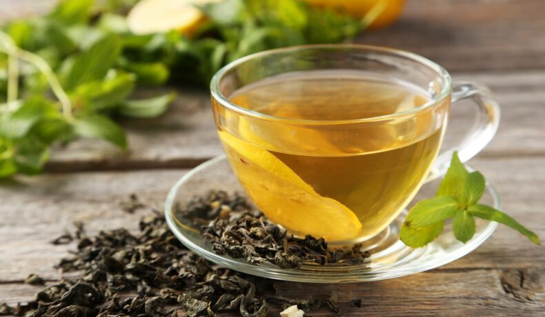 Ceașcă de ceai transparentă, pe o farfurie, cu frunze de ceai, o masă din lemn. Experții au dezvăluit recent detaliul ascuns din ceai