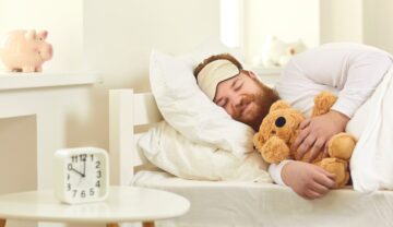 Bărbat cu barbă roșcată care doarme cu un ursuleț în brațe. Experții cred că o nouă tehnologie poate să ajute oamenii să slăbească în timp ce dorm