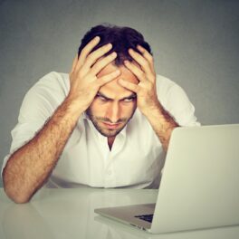 Bărbat nervos în fața calculatorului, pe fundal gri, similar cu investitorul care a pierdut 150.000 de dolari pe o glumă NFT