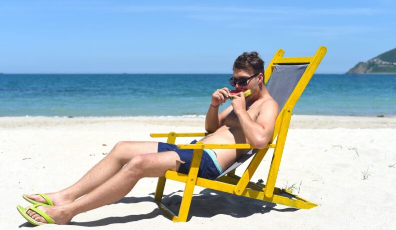 Bărbat care mănâncă pepene pe plajă, într-un șezlong galben, mâncând pepene. Apetitul bărbaților crește la plajă, susțin experții