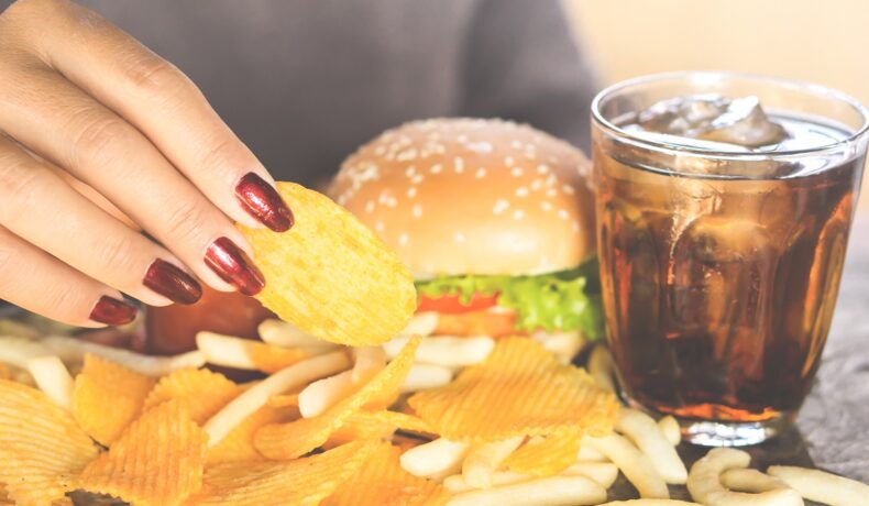 Femeie care mănâncă chipsuri, burger și bea suc, unele dintre cele mai dăunătoare alimente pentru dinți