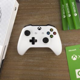 Consolă Xbox One pe alb, pe o masă din lemn. Acum, Microsoft recunoaște că vânzările Xbox One au fost mai mici decât cele PS4