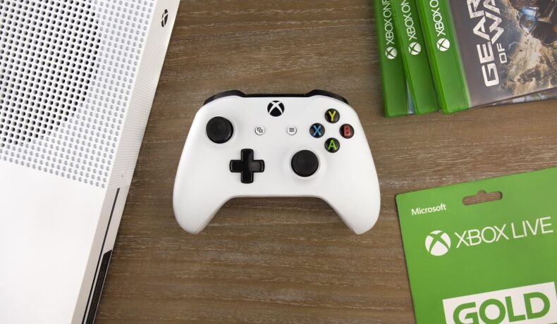 Consolă Xbox One pe alb, pe o masă din lemn. Acum, Microsoft recunoaște că vânzările Xbox One au fost mai mici decât cele PS4