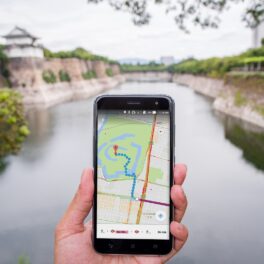 Utilizator care ține un telefon cu Google Maps în mână, în fața unui râu. O familie s-a pierdut în sălbăticie 48 de ore din cauza Google Maps