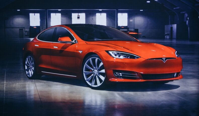 Mașină Tesla portocalie, pe fundal gri. Musk a dezvăluit recent cât va costa sistemul Tesla full self-driving