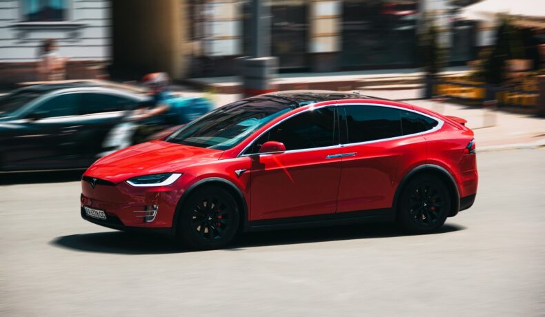 Mașină Tesla roșie pe drum. Unii proprietari Tesla își îun copiii în fața mașinilor