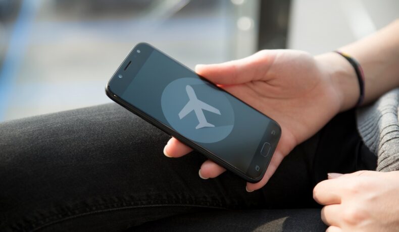 Utilizator care are un smartphone în mână, cu modul avion pe ecran, pe care trebuie să îl folosești în timpul zborului