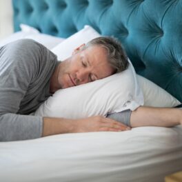 Bărbat care doarme în pat, cearșafuri albe, tăblie albastră. Experții au dezvăluit ce ți se poate întâmpla dacă dormi mai puțin de 5 ore pe noapte