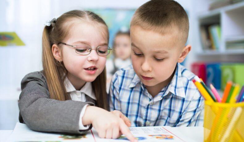 Fetiță și băiat în clasă, care se uită pe o carte. Experții au dezvăluit de ce dau profesorii note mai mari fetelor