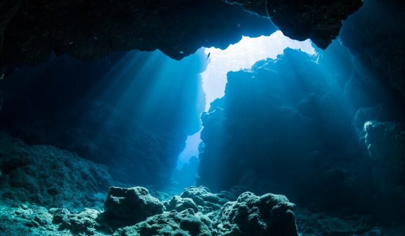 Imagine din ocean, cu lumina care se strecoară printre stânci, similar cu un ocean sub suprafața Pământului