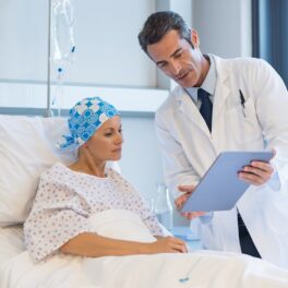 Doctor care vorbește cu o pacientă, care stă în pat, posibil depre o epidemie de cancer