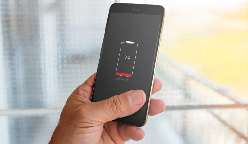 Utilizator care ține un telefon negru în mână, cu bateria telefonului scăzută, ce poate fi afectată de obiceiuri de încărcare care îți distrug bateria